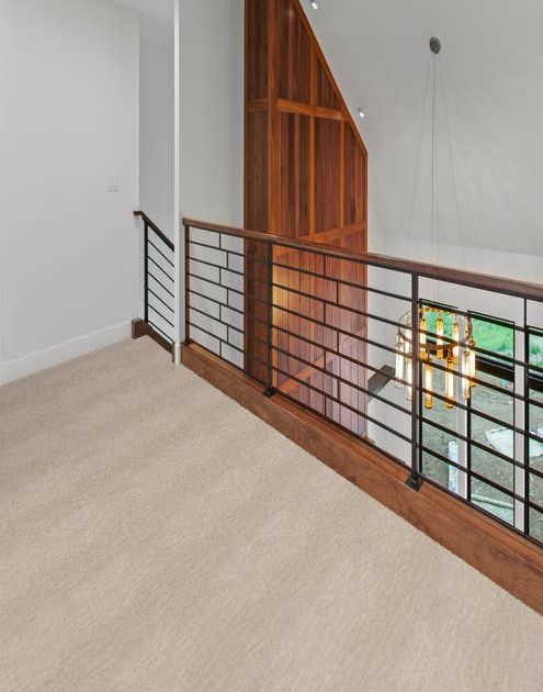 Alistair Stone colored carpet in hallway with white walls and a wooden accent wall with black stair railing.
