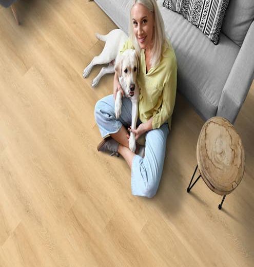 Woman with dog on her lap sits on a light-color wood-look LVP and leans against a modern gray sofa