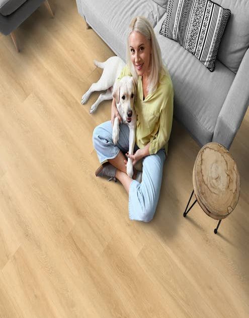 Woman with dog on her lap sits on a light-color wood-look LVP and leans against a modern gray sofa