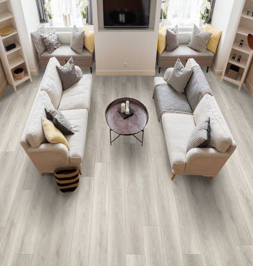 Living room with two couches facing each other, a television on the wall, window seats, and vertical bookcases, over light gray wood-look vinyl plank flooring