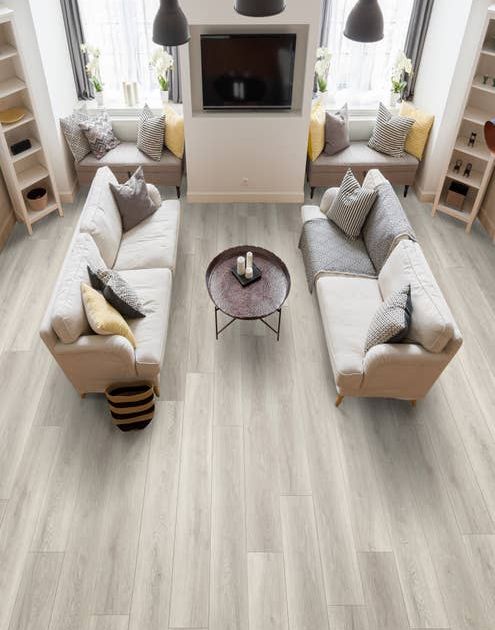 Living room with two couches facing each other, a television on the wall, window seats, and vertical bookcases, over light gray wood-look vinyl plank flooring