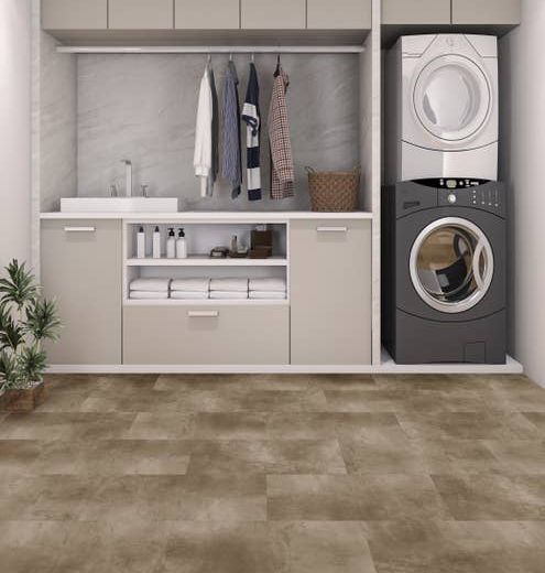 Laundry room with built-in light gray cabinets, stacked white/gray washer and dryer, and hanging shirts with gray and tan concrete-look LVT