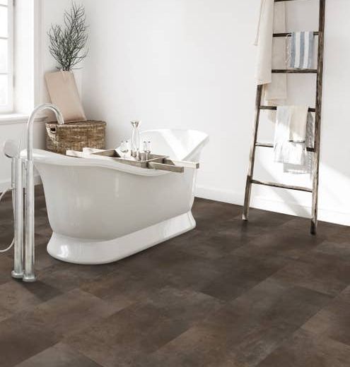 Modern white bathroom with a white free-standing bathtub, a rustic ladder shelf with towels, and a brown tile-look LVT floor