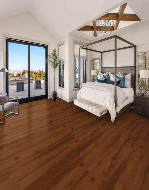 Bedroom with four-poster bed, dark cherry luxury vinyl plank floors, and a set of sliding glass doors overlooking an outdoor patio