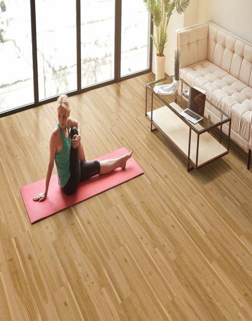 Woman on pink yoga mat stretches beside floor-to-ceiling windows, glass coffee table, and cream sofa