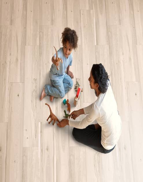 Mother and child play on light beige woodgrain laminate and play with toy dinosaurs