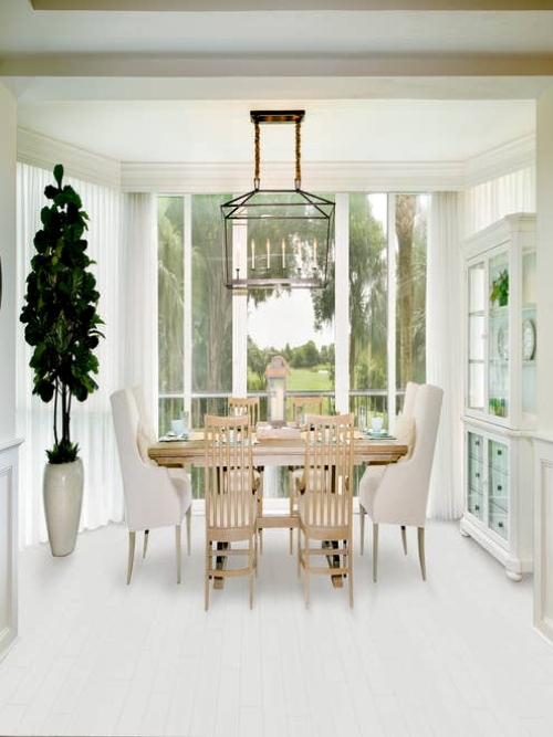 Bright, airy room with floor-to-ceiling windows overlooking yard, with large chandelier, potted tree, and dining room table set beside white display cabinet