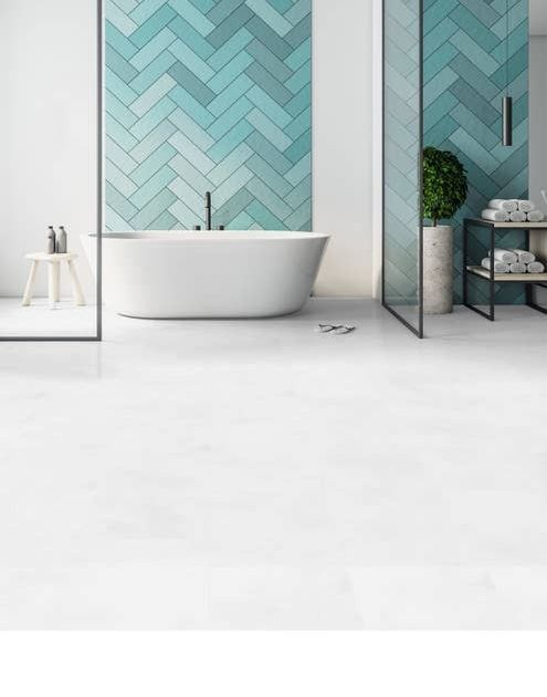 Free-standing white bathtub set against a wall with various shades of light blue herringbone tile and bright white tile LVT flooring