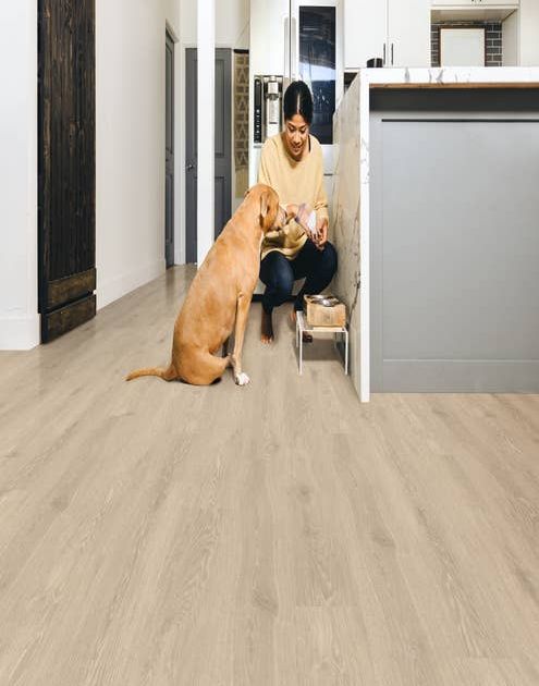 Woman crouches and feeds dog at end of kitchen island on cream woodgrain floor