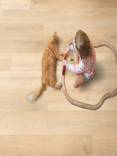 Young girl sits inside toy wooden train track beside orange striped cat