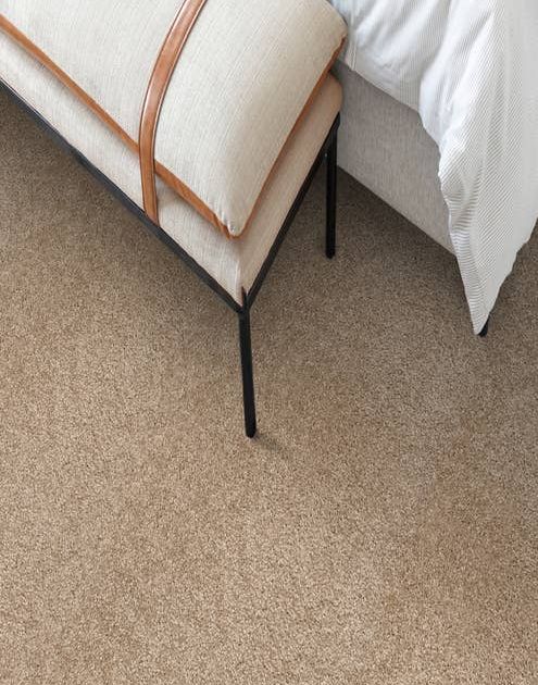 Overhead photograph of ottoman at end of bed, on tan solid plush carpet