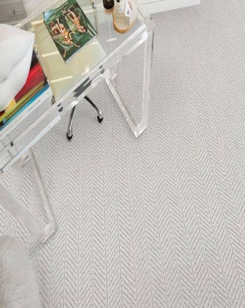 Modern glass desk with magazines on a light gray chevron patterned carpet