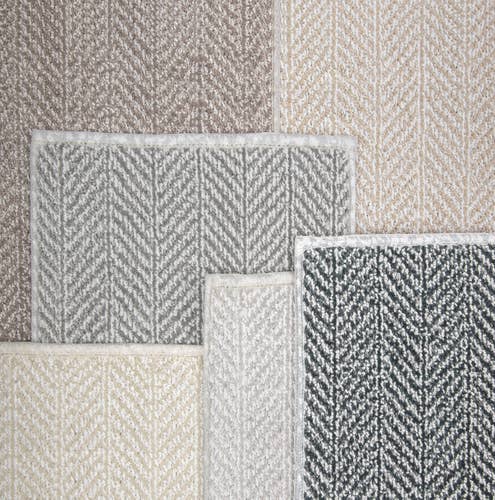 Staggered pile of multiple gray, tan, blue, and cream linear/geometric patterned carpet samples