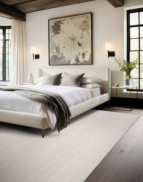Modern bedroom scene with bed, moder artwork, dark wood floors, and a light gray textured area rug