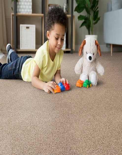 Young boy plays with toy cars and dog stuffed animal on a tan solid carpet