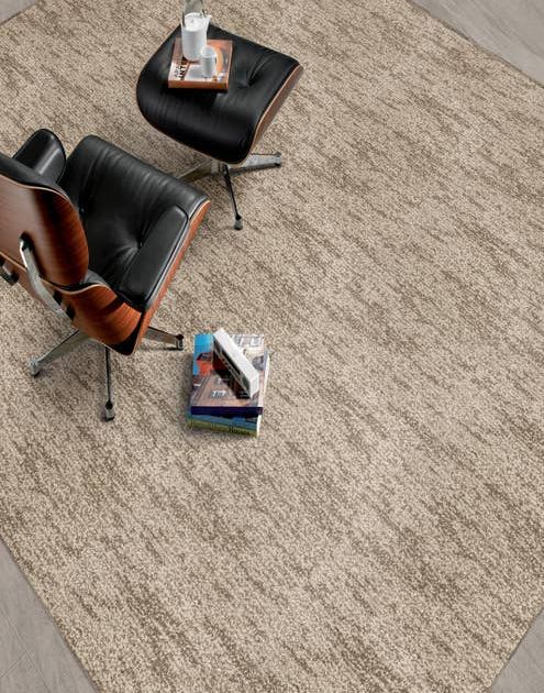 Modern leather chair and ottoman and stack of books on a abstract patterned textured taupe carpet.