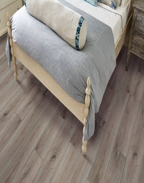 Inviting bed, with pale blue comforter, large pillows, and rustic wooden frame on weathered beige LVP