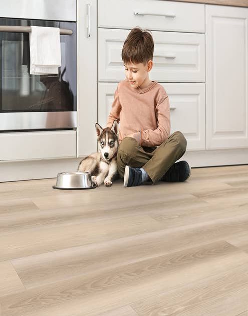 Young boy and husky puppy sit on kitchen floor before white cabinets and light woodgrain vinyl flooring