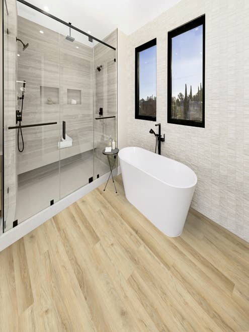 Luxury bathroom with walk-in shower, free-standing bathtub, beige woodgrain plank flooring, and windows showing neighborhood beyond