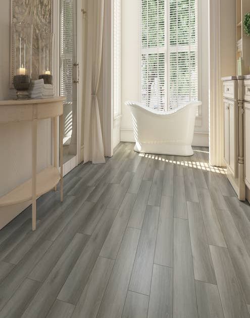 Airy, spa-like bathroom with free-standing tub before large window, with medium and light gray plank flooring