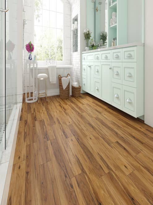 Bathroom with large vanity, glass shower door, and white bathtub before bright window, with golden brown LVP floors