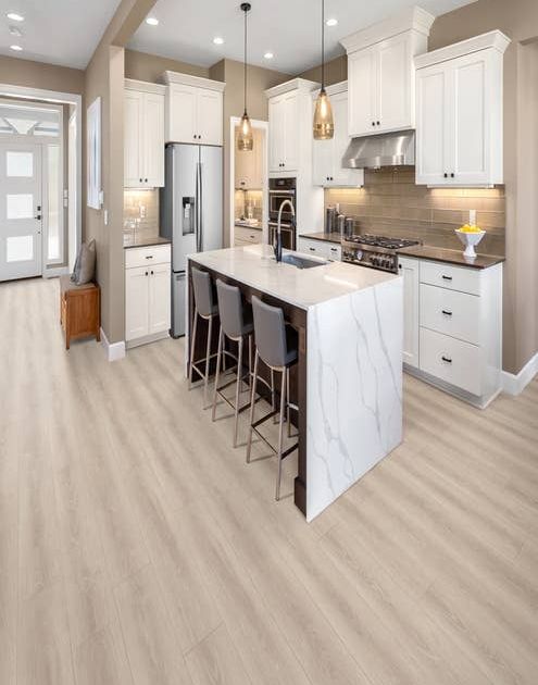 Small modern white kitchen with marble-topped island, seating, with view of entry hall, over light gray woodgrain laminate