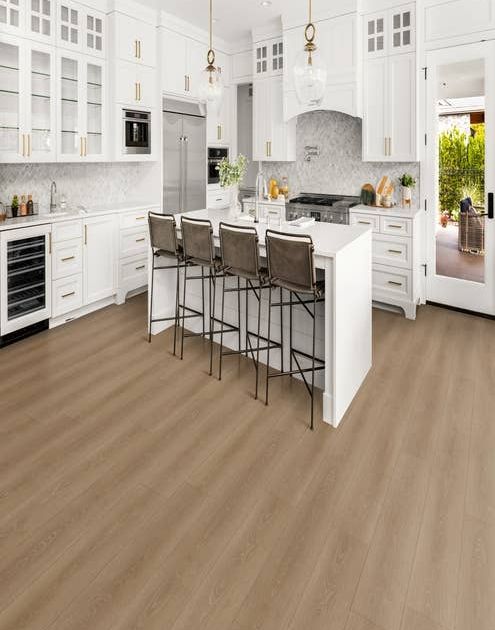 Luxury modern white kitchen with gold accents, with island seating area, over warm brown woodgrain laminate, with view of side porch