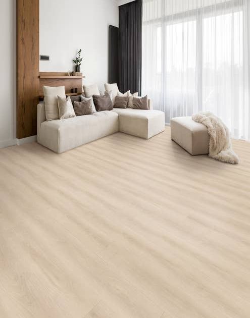 Cozy, bright, airy room with couch laden with pillows and a fur blanket, on cream woodgrain floor