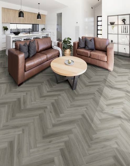 Modern open concept living area and kitchen, featuring light/medium gray herringbone floor, leather couches, and white walls