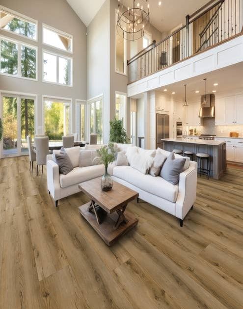 Open-concept living room, kitchen, and dining area with beige weathered floors and large windows showing wilderness beyond,