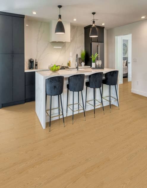 Clean sophisticated kitchen featuring navy blue cabinets, white marble backsplash, and island with velvet barstools, over warm, tan-toned woodgrain floor