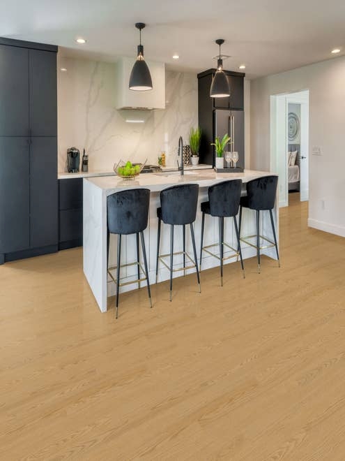 Clean sophisticated kitchen featuring navy blue cabinets, white marble backsplash, and island with velvet barstools, over warm, tan-toned woodgrain floor