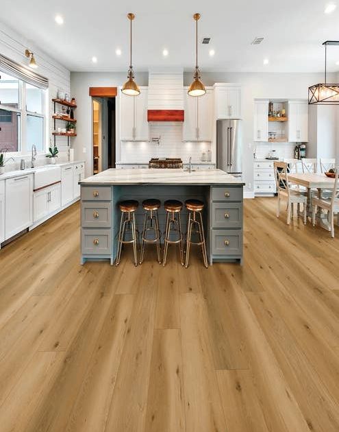 Blue kitchen island with barstools, white cabinetry, gold pendant lights, and warm tan oversized luxury vinyl planks