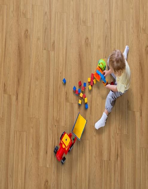 Boy sits on warm, gold laminate floor and plays with toys