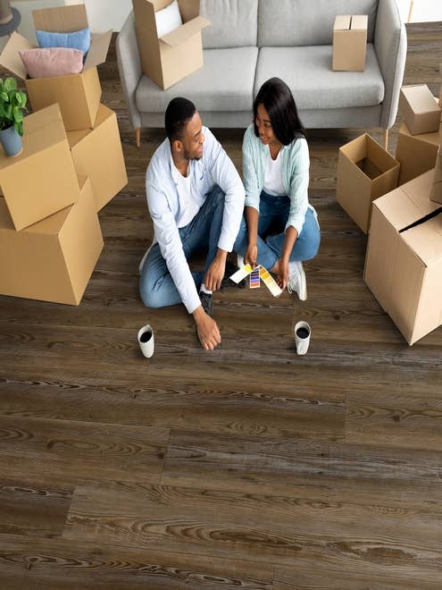 Young couple sits amid pile of moving boxes stacked on Pinehill Bark luxury vinyl plank floor