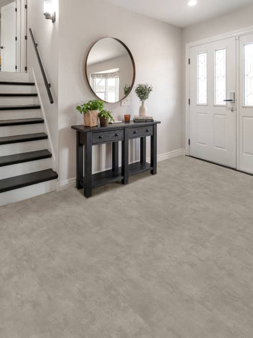 Split-level entryway with white walls, light gray stone luxury vinyl tile flooring, a black entry table, and large round mirror