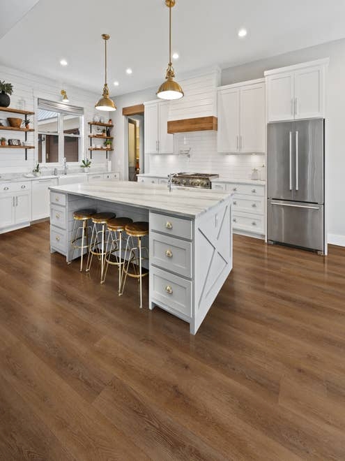 Modern farmhouse kitchen with white cabinetry and island, barstools, pendant lights, and wooden accents over a medium brown woodgrain luxury vinyl plank floor