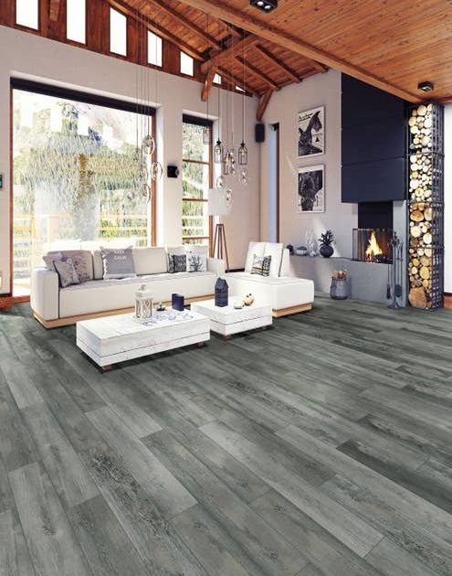 Living room with white sectional, tall wood ceilings, firewood stacked beside modern fireplace, glass pendant lighting, and blue-gray woodgrain Rockwood Bluestone flooring, with large windows showing outdoors