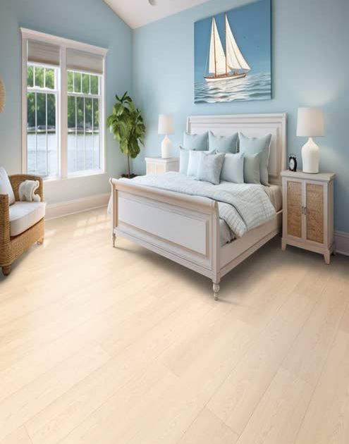 Bright, airy bedroom with bed, nightstand, corner chair, potted plant, and sailboat painting with light blue walls and pale woodgrain floor