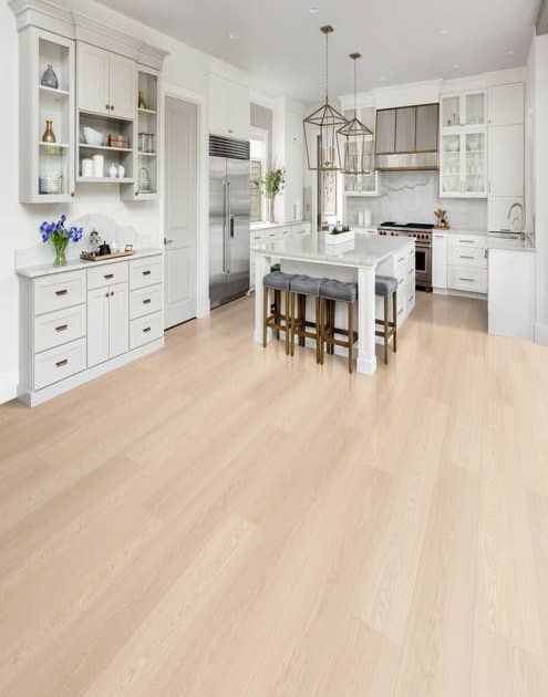 Modern white kitchen with oversized metal chandeliers, central island with seating, and pale beige woodgrain LVP floors