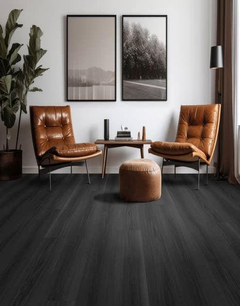 Two leather chairs, a small table, an ottoman, and a potted plant on a black woodgrain floor, in room with two black and white photos on white wall