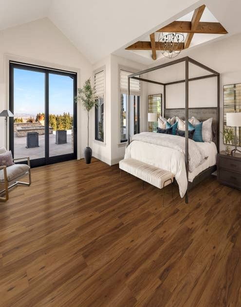 Bright, airy bedroom with large bed, nightstand, and armchair, over LVP floor with varying brown tones, with large glass doors leading to patio