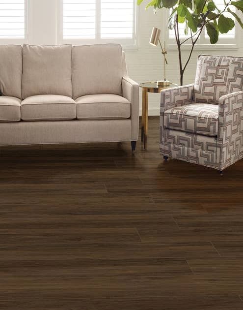 Couch, armchair, and houseplant in bright living room with dark, rich woodgrain LVP floor