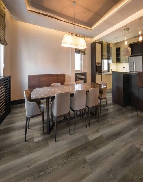 Dining table and chairs near black kitchen cabinets, with recessed lighting, rectangular chandelier, with medium gray woodgrain LVP floors, in cozy, moody space
