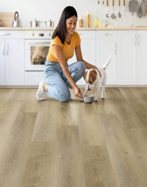 Woman kneels before modern white kitchen cabinets with wooden countertops and feeds small dog