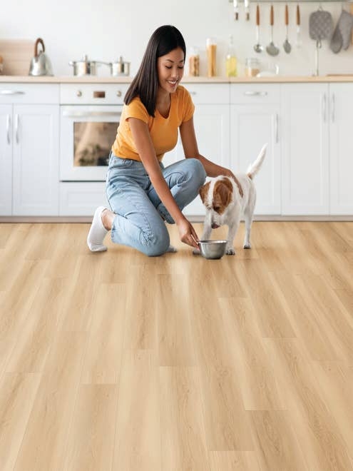 Woman kneels before white kitchen cabinets and gives small dog food bowl