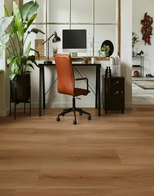 Home office with leather chair, computer desk, storage cabinet, and large potted plant in room with natural light a rich, warm wood-look LVP flooring