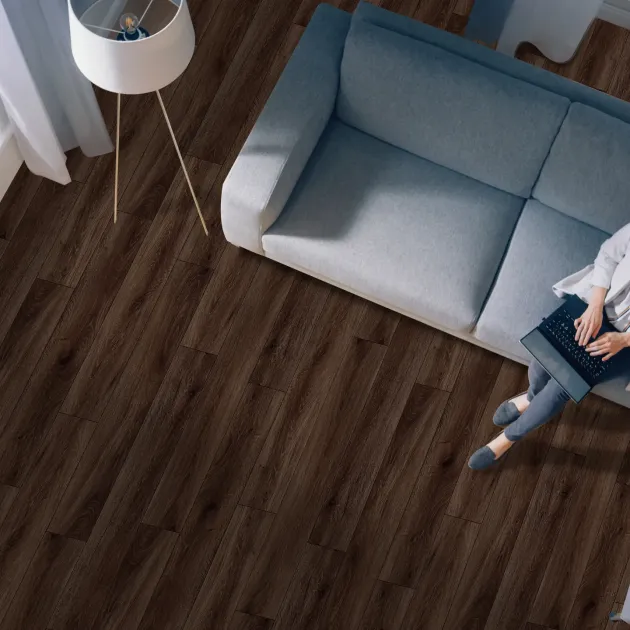 Woman sits on couch and works on laptop beside floor lamp, in calming room with blue walls and rich walnut-color LVP floor
