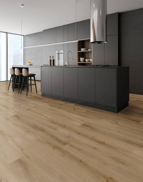 Minimalist kitchen with black cabinetry and island, silver range hood, with extended seating bar and chairs, over tan wood-pattern LVP