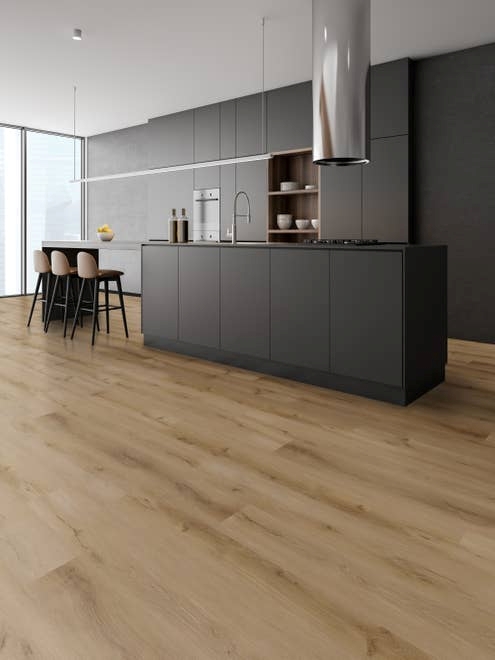 Minimalist kitchen with black cabinetry and island, silver range hood, with extended seating bar and chairs, over tan wood-pattern LVP